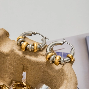 Minimalist 18K gold and stainless steel multi-hoop earrings on textured beige display