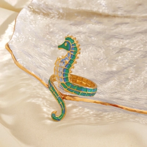 Golden seahorse ring with green and blue enamel details on an elegant glass tray