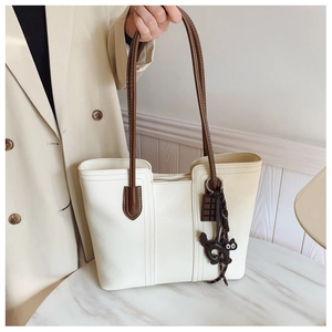 Detail view of white leather tote bag with brown straps and a cute cat charm