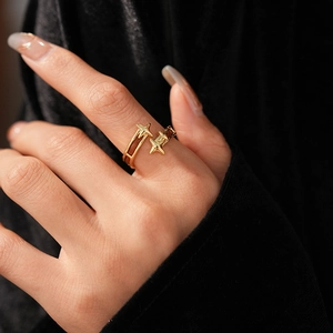 Détail de la bague ouverte double étoile dorée vintage sur main avec velours noir élégant