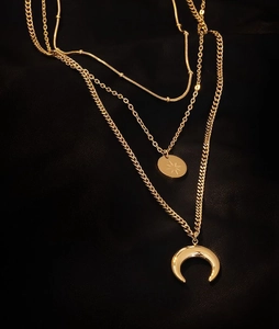 Detail of gold multilayered necklace with star coin and moon pendants on dark silk