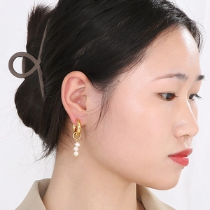 Detail view of gold hoop earrings with three white pearls worn by a model in soft light