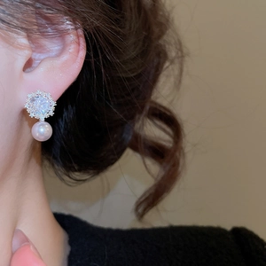 Close-up of elegant pearl earrings with sparkling floral cubic zirconia studs on ear