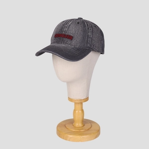 Detailed view of red CONQUER embroidery on a vintage washed grey denim baseball cap