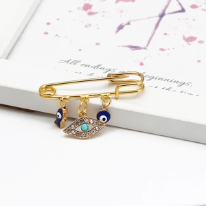 Detail of gold safety pin brooch with sparkling blue evil eye and palm charms