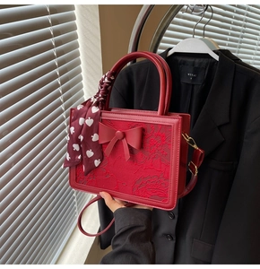 Close-up of a red lace handbag featuring a bow decoration and a patterned silk scarf