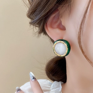 Close-up of elegant gold-plated cat eye stone earrings with green enamel on a model