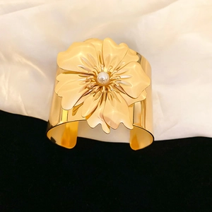 Macro shot of large golden metal flower bracelet featuring a central pearl accent