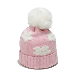 Close-up of pink knitted hat with white floral embroidery and soft fluffy pom-pom detail