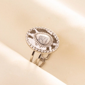Macro view of textured oval silver ring with white marble teardrop stone on beige fabric