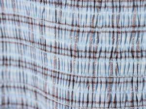 Macro shot of blue and brown plaid fabric with elastic smocked texture and precision stitching