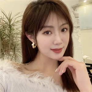 Gros plan de boucles d'oreilles créoles dorées irrégulières portées par un mannequin chic