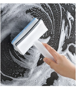 Close-up of a handheld glass squeegee cleaning foam off a surface with a blue sponge side