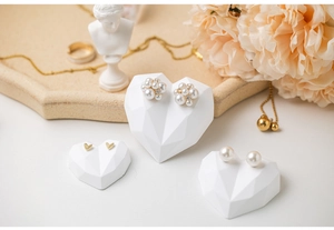 Close-up of pearl cluster and golden heart earrings on creative white display stands