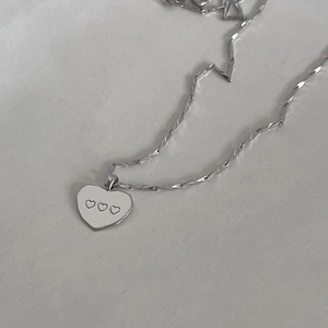 Macro shot of silver heart pendant featuring three small engraved hearts on flat metal chain