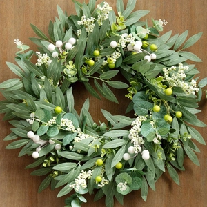 Detailed close-up of artificial olive leaf wreath with white berries on wood background