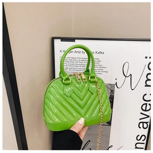 Close-up of a glossy green shell-shaped bag with V-shaped stitching and gold chain