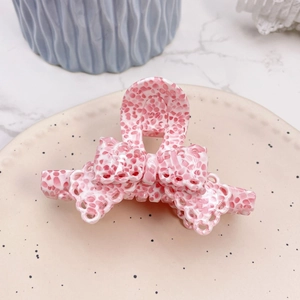 Close-up of pink floral acetate hair claw with delicate lace bow design on ceramic plate