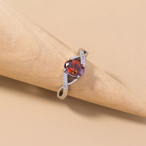 Detail view of a silver ring with oval red gemstone and twisted band on wood stand