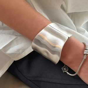 Detailed view of wide silver bangle with brushed metal finish on model's wrist