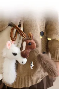 Detail of plush pony head pendants with pullable tails on a beige shoulder bag