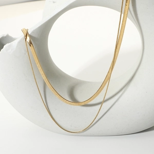 Detail of a layered golden herringbone and round snake chain necklace on white prop