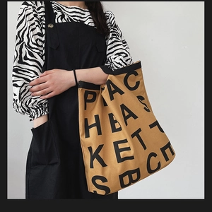 Close-up of khaki canvas tote bag featuring black letter print and texture on a shoulder strap