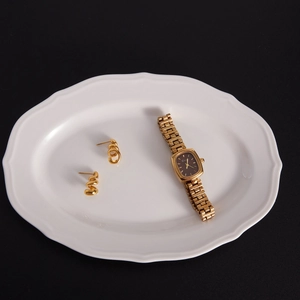 Vue à plat de boucles d'oreilles spirales en or 18K et d'une montre dorée sur une assiette
