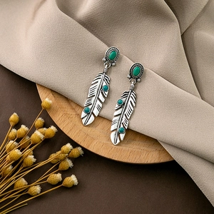 Detail of vintage feather earrings with turquoise beads on a silk fabric background