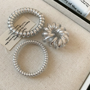 Three-piece set of silver metallic spiral hair ties on a premium textured beige fabric