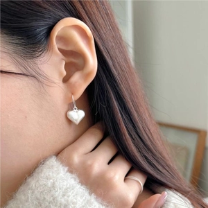 Detail view of heart-shaped silver earrings with a matte brushed finish on female model