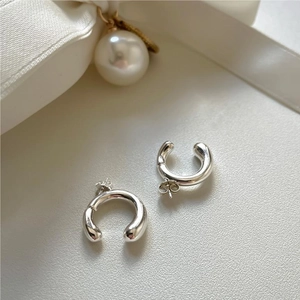 Macro view of minimalist 925 sterling silver C-shape hoop earrings on white silk ribbon
