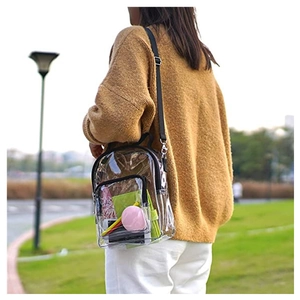 Transparent PVC mini crossbody bag with black straps worn by model in a lush park setting