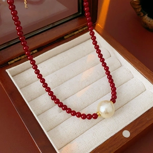 Détail d'un collier de perles rouges avec perle centrale présenté dans un coffret