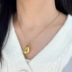 Close-up of a golden teardrop pendant necklace worn by a model in stainless steel finish