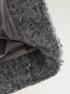 Macro view of grey curly faux fur texture and dark grey lining on a cropped wool jacket