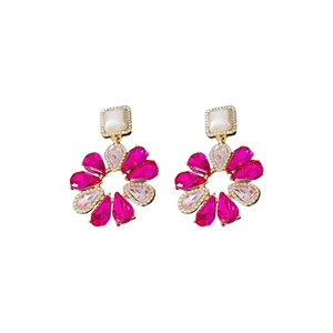 Orecchini a fiore dorati con cristalli rosa acceso e pietre bianche su sfondo bianco