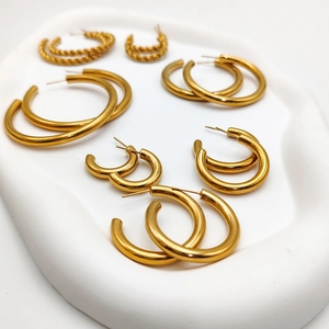 Macro detail of various gold-plated stainless steel hoop earrings in a ceramic tray