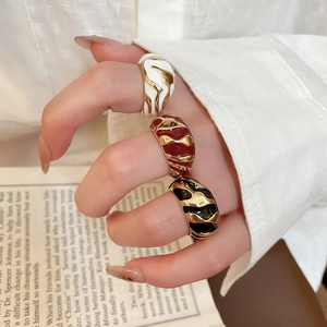 Detailed view of three wide enamel rings in white, red, and black with wavy gold texture