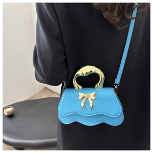 Detail of blue bow handbag featuring a unique wave bottom and gold fluid handle