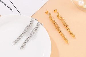 Dettaglio degli orecchini lunghi a catena in oro e argento con scritte LUCK