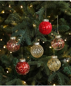 Detail of red and gold glitter Christmas balls hanging on tree branch with warm lights