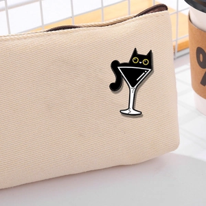 Cute black cat enamel pin in a martini glass displayed on a beige canvas backpack bag
