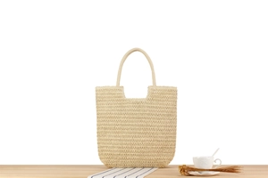 Detail of handwoven beige straw tote bag on a wooden table with rustic vacation props