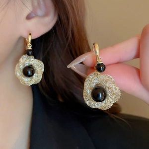 Detail of woven gold wire earrings with black bead accents shown on an ear