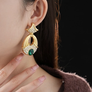 Close-up of luxury gold ginkgo leaf earrings with green emerald stone and crystals on model