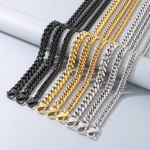 Polished Cuban chain necklaces in black, gold, and silver on grey cylindrical displays