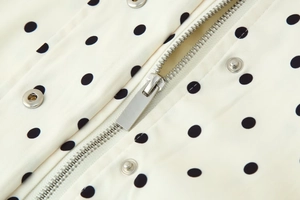 Detail view of silver metal zipper and snap button on black polka dot print jacket