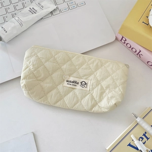 Détail de la trousse matelassée beige avec charme de cœur et étiquette de chien