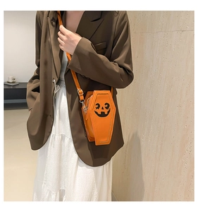 Close-up of orange coffin-shaped crossbody bag with pumpkin face on a female model